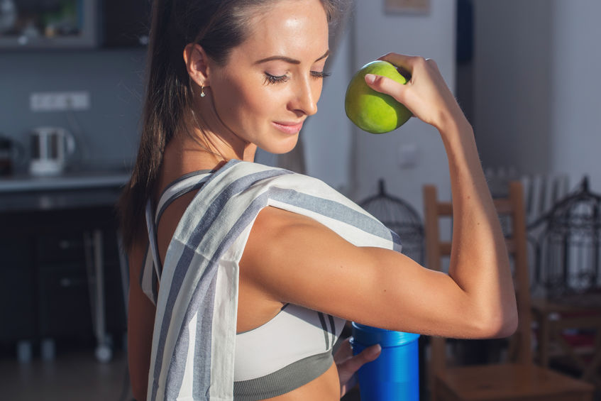 Active athletic sportive woman with towel in sport outfit holding apple showing biceps healthy lifestyle