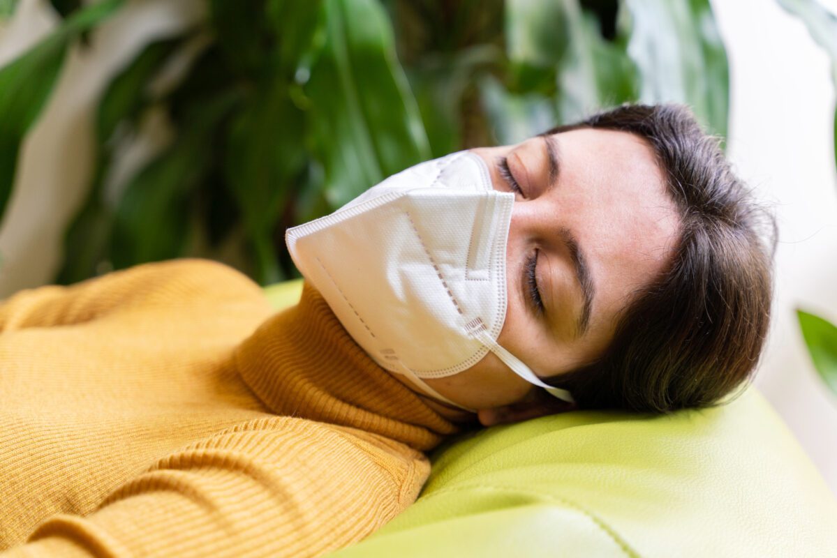 Horizontal portrait of woman infected with coronavirus disease sleeping in the couch at home. Stay home. Pandemic worldwide virus disease covid 19. Health issues concept. Sick woman with face mask.